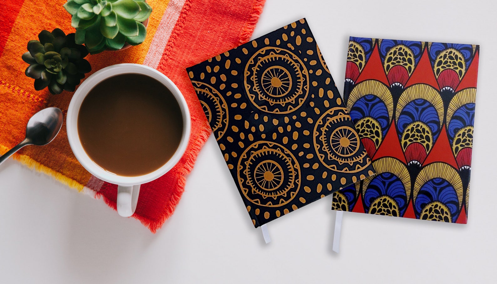 Two richly-colored notebooks beside a cup of coffee on a table. 