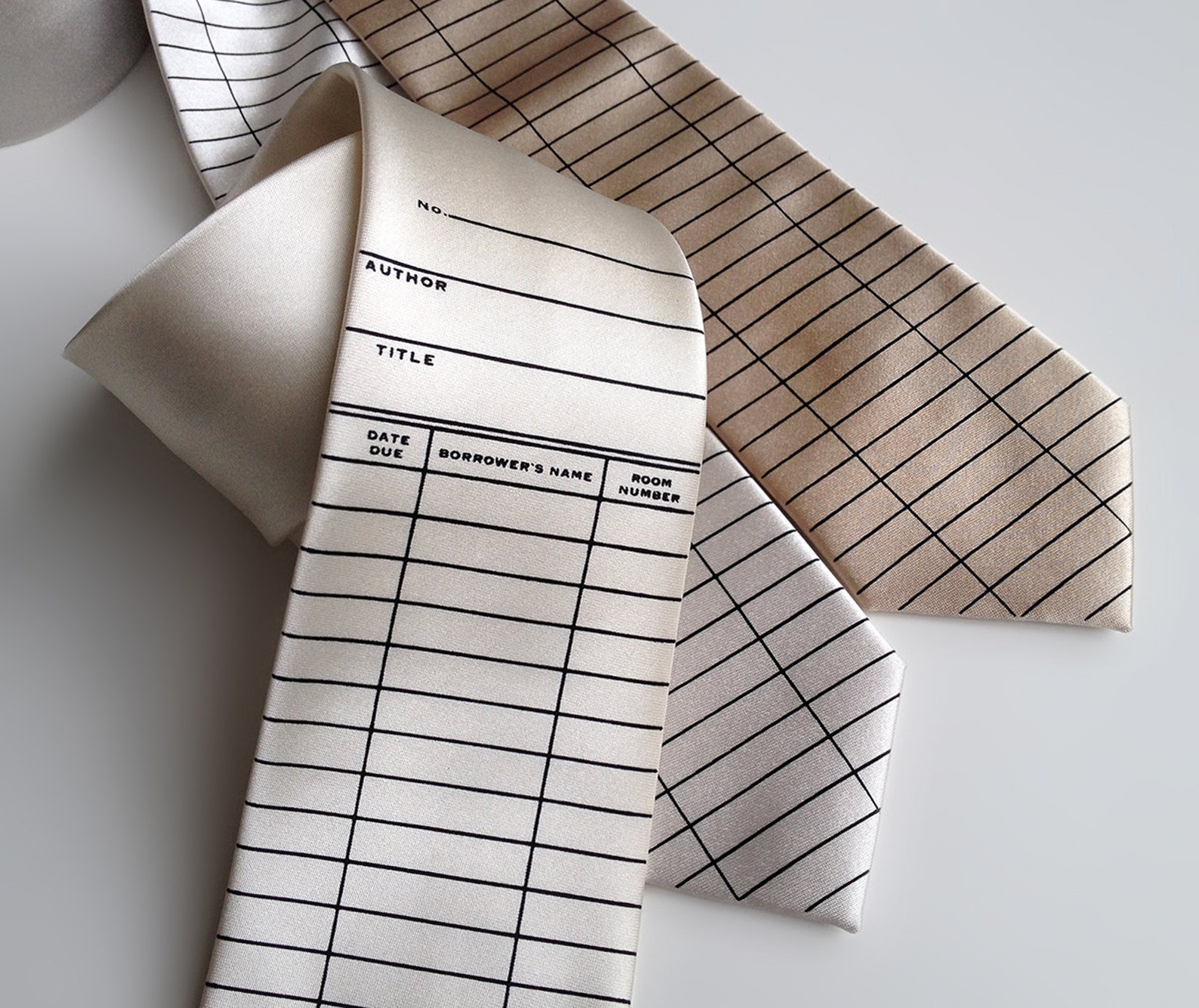 Image of three neckties with a due date pattern. All of the ties are cream colored and the text is black. 