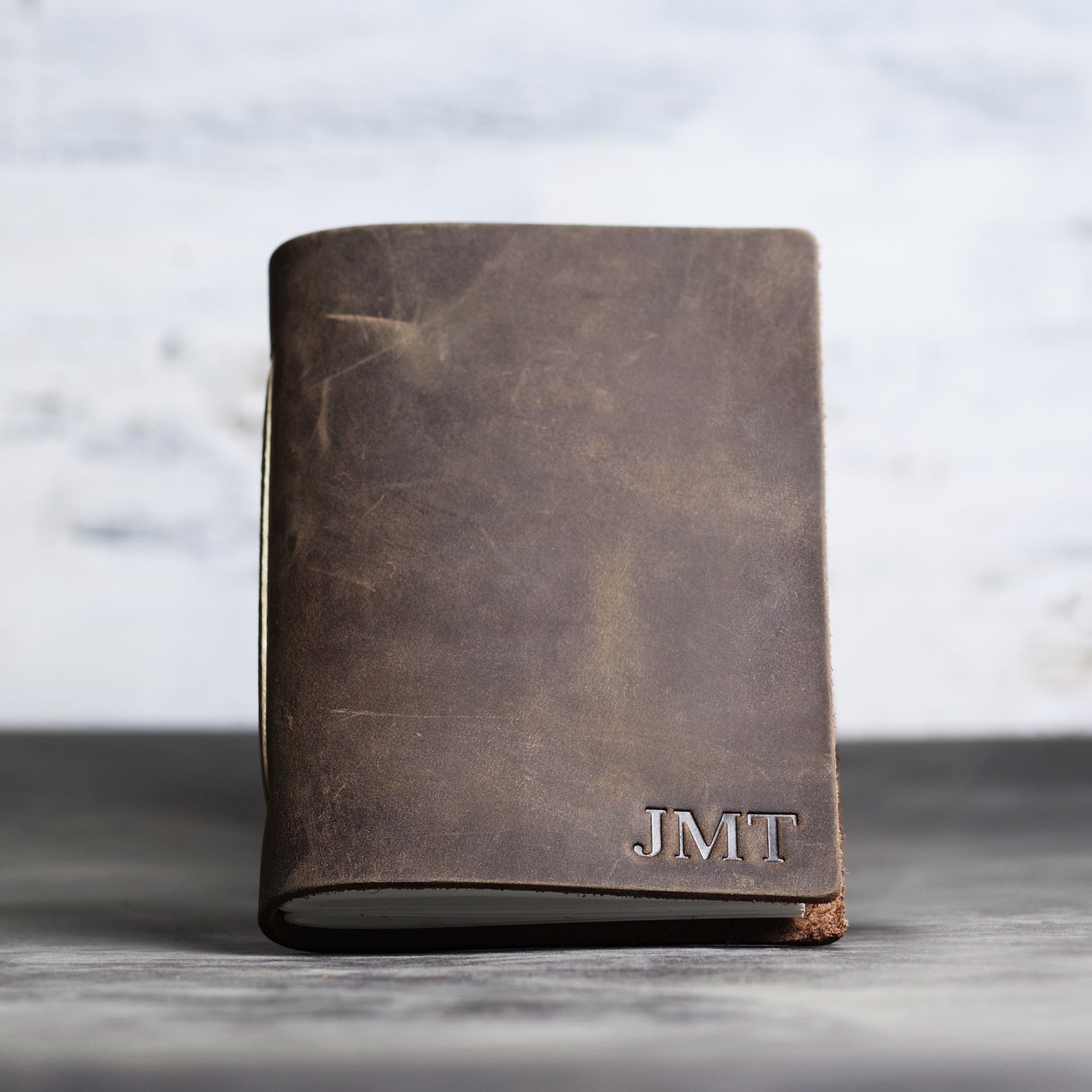 Image of a brown leather notebook with the initials JMT on the bottom right. 
