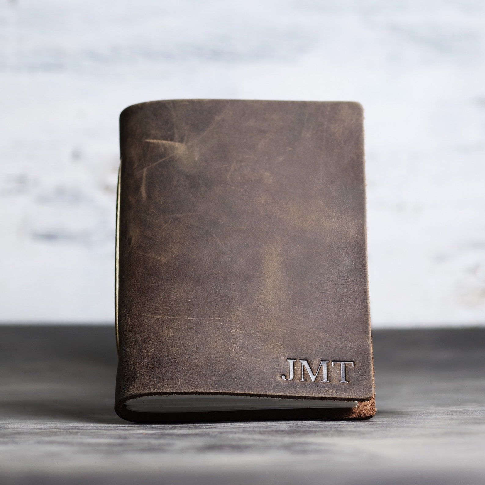 Image of a brown leather notebook with the initials JMT on the bottom right. 