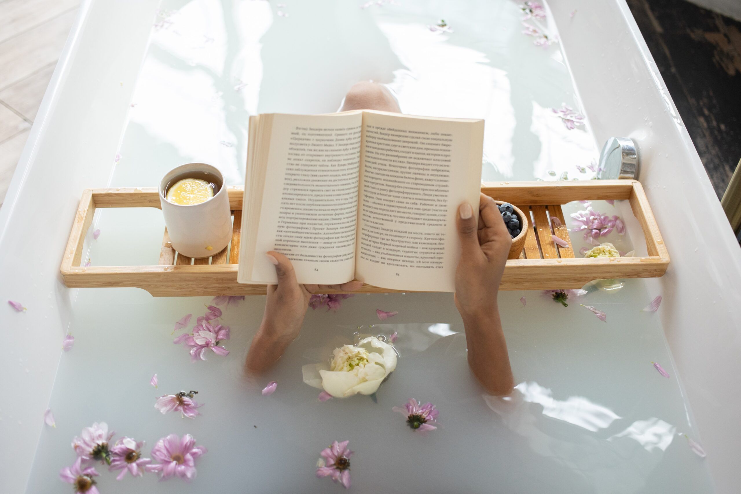 A photo of someone reading in the bath with candles and flower petals