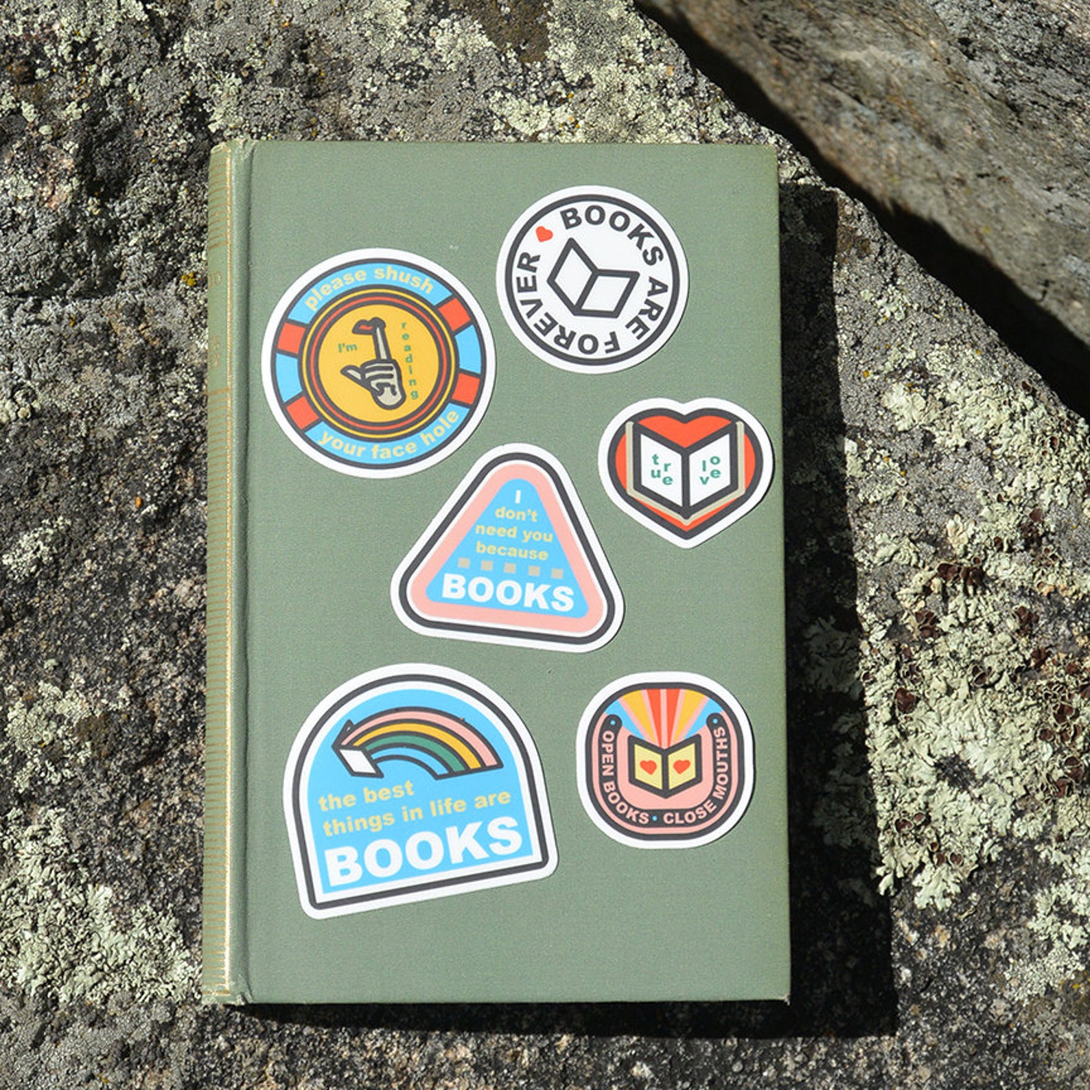 Six vintage-style book stickers on a green hardback book. The book is on concrete. 