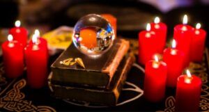 Image of a crystal ball on a stack of books between lit red candles