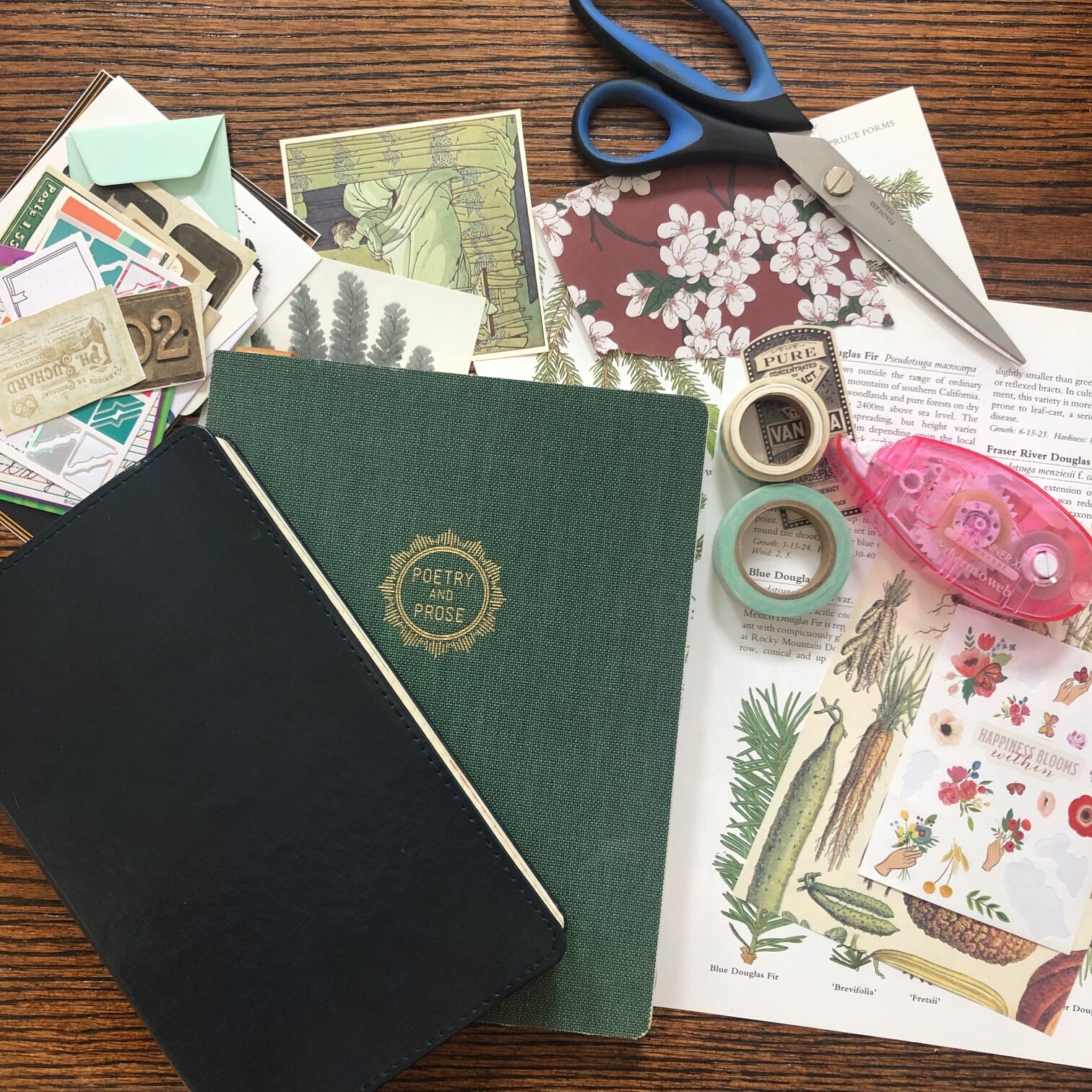 Image of two journals on a table, surrounded by supplies for junk journaling: a tape roller, scissors, tape rolls, and lots of paper and stickers. 