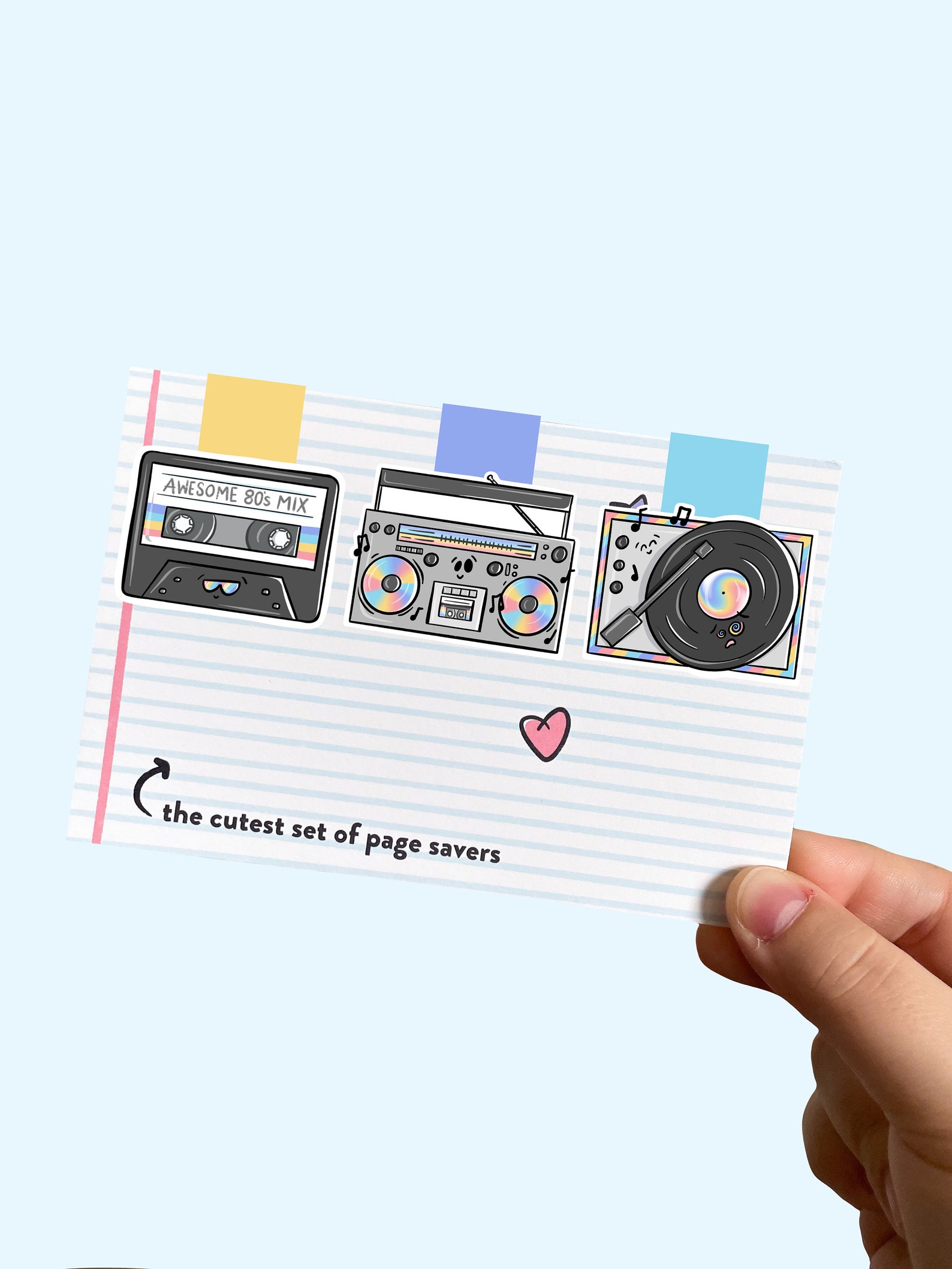 Image of three magnetic bookmarks on an index card. It is being held by a white hand. The images of the bookmarks are a mix tape, a boom box, and a record player. 