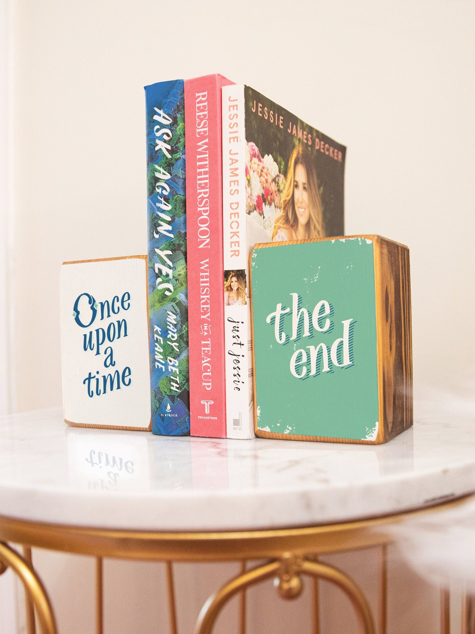 Two wooden blocks printed with the words "Once Upon a Time" and "the end" hold up three books.