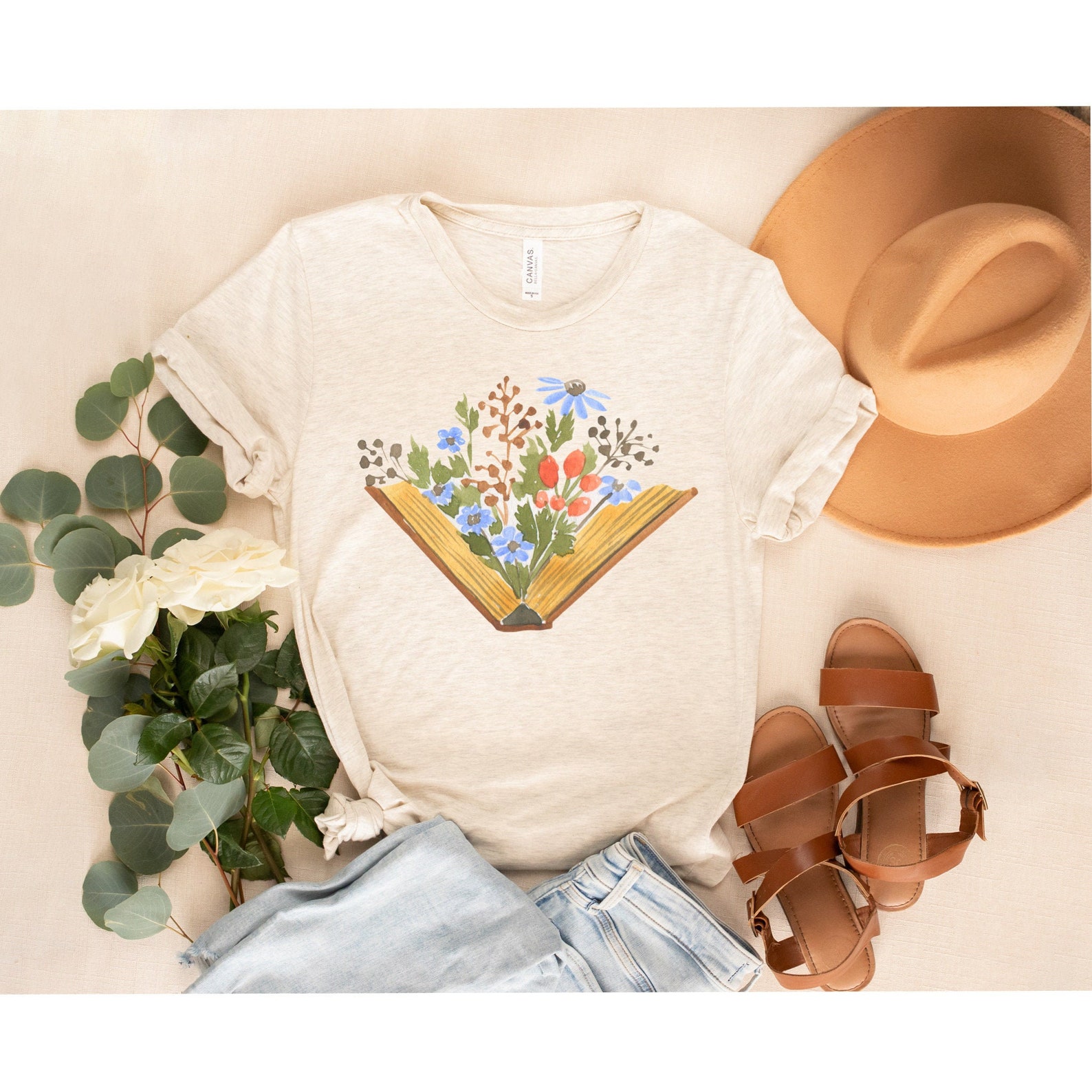 A cream t-shirt depicting an open book with florals springing from the pages