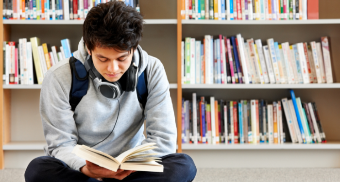 A photo of a teenager sitting on the floor of a library reading