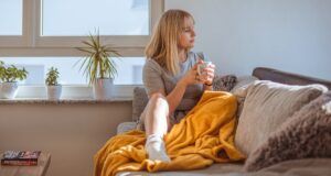 a photo of a woman under a blanket holding a mug