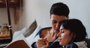 two women snuggling on a couch, with one reading