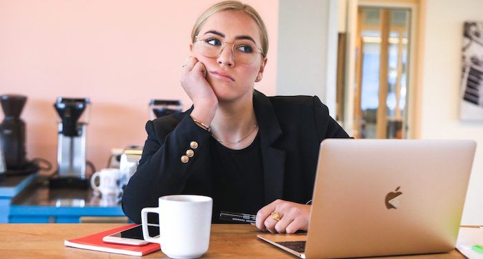 a photo of someone resting their head on their hand, looking at their laptop unhappily