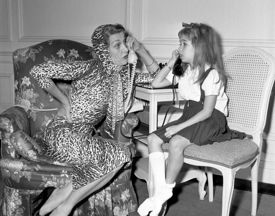 A black and white photo of Kay Thompson and Evelyn Rudie Eloise sitting next to each other, each holding a telephone and talking to each other