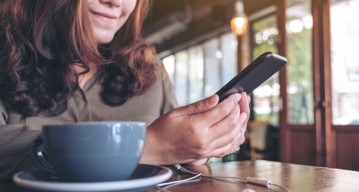 Image of a person with a coffee mug in a cafe reading on phone