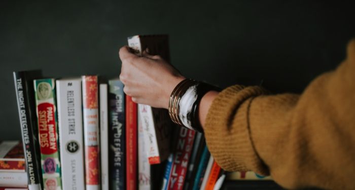 pale skinned hand white and red book on bookshelf