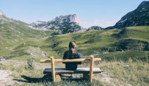 a photo of a person sitting on a bench looking out as grassy hills