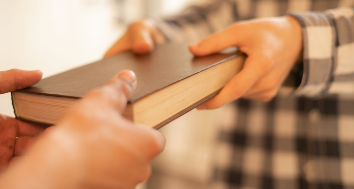 the hands of two people exchanging a book