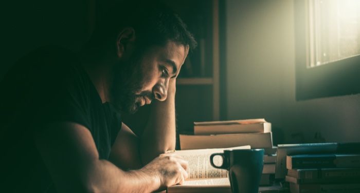 a person with tan skin reading near a window with sunlight pouring in