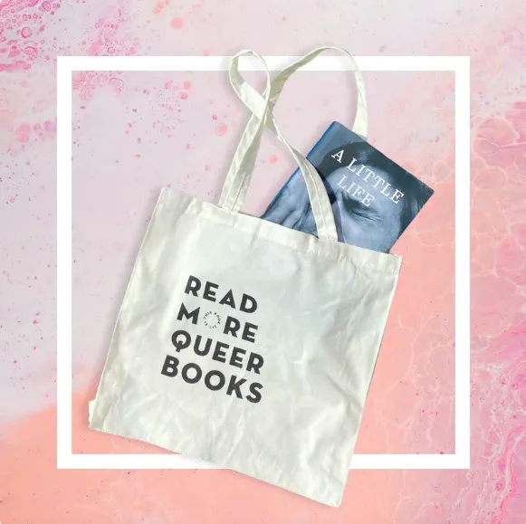 Tote bag that says "Read More Queer Books" with the book A Little Life partway out of the bag 