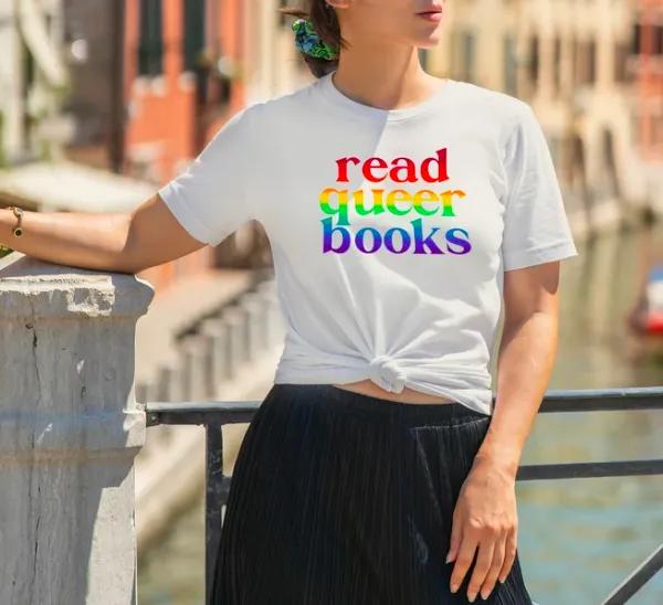 Photo of woman modeling a white t-shirt with "read queer books" in screenprinted in rainbow font