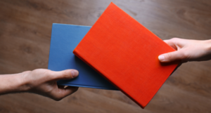 a photo of two people holding out books to each other, only their hands visible