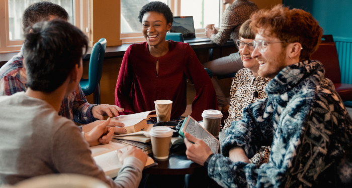 a photo of several people at a coffee shop laughing and talking while holding books