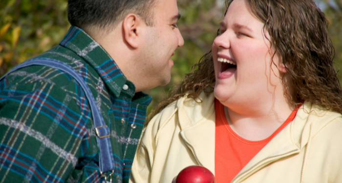 a photo of a fat white man and woman laughing together in an apple orchard