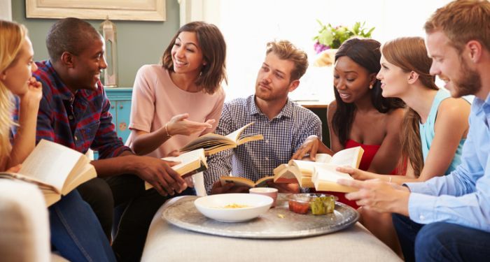 group of people of different skin tones gathered around a table discussing books