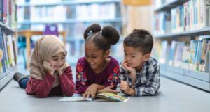 Image of three children reading on the floor between bookshelves