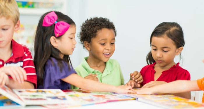 four small children reading picture books in a school setting