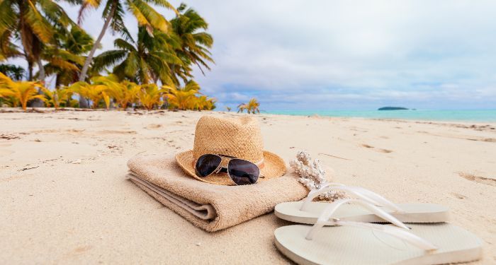 sunglasses, a beach towel, and flip flops arranged n the beach