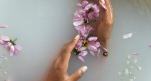 brown hands in cloudy water with floting purple flower petals