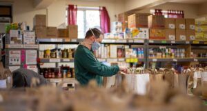 a photo of someone wearing a mask looking at bags of food at a community food pantry