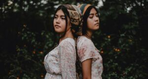 two brown-skinned women with dark features standing back to back