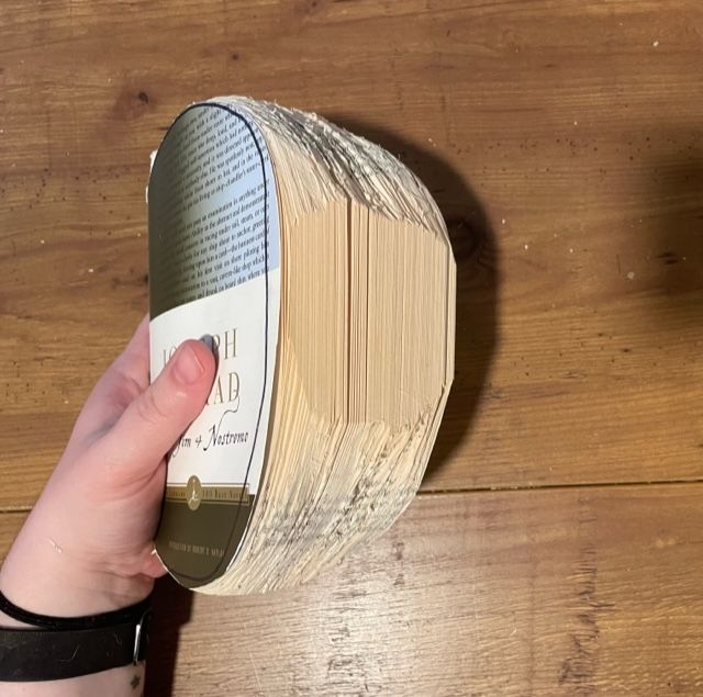 A hand holds a book that has been carved into the shape of half of a pumpkin