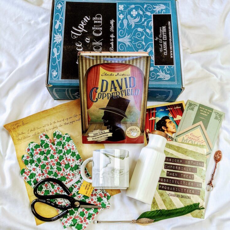 a photo of a Once Upon a Book Club book subscription box with gardening gloves, shears, a mug, and other goodies