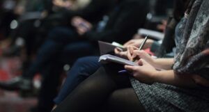 the legs of a row of seated people taking notes in notebooks