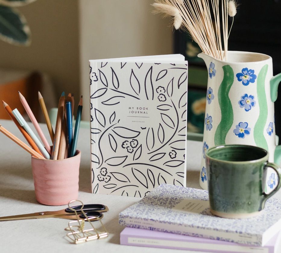 Image of "my book journal" between a table scape with a coffee mug, pitcher, colored pencils, and a binder clip. 