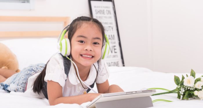 Image of an Asian girl wearing headphones on a bed with a tablet