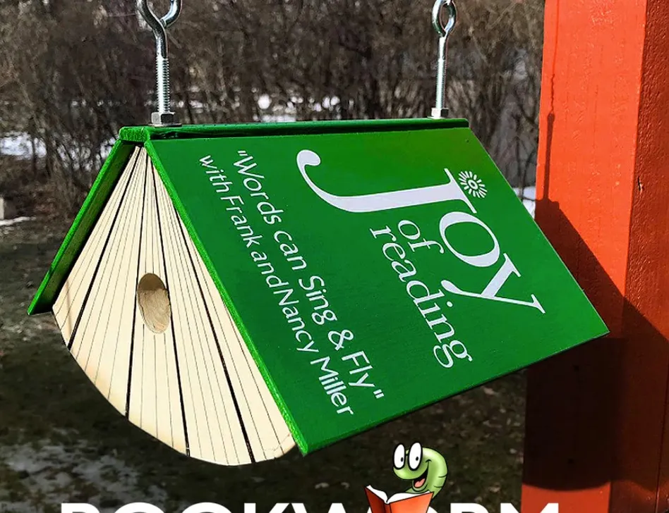 Image of a green birdhouse in the shape of a book. The book is titled "Joy of Reading."