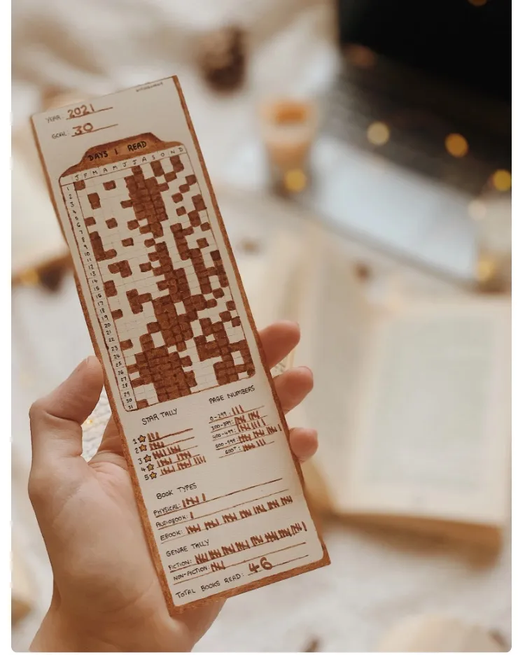 Image of a bookmark that allows you to track your reading habits. It is being held by a white hand.