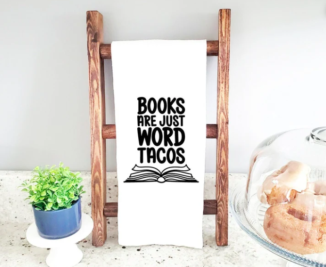 Simple white tea towel displayed with screen printed in black: "Books are just word tacos" and an open book illustration