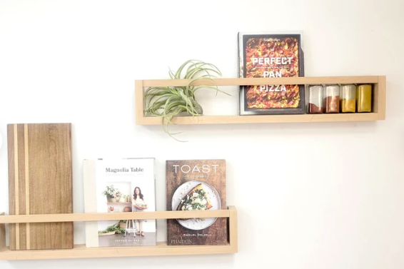 Simple wooden display racks on a wall with various cookbooks and spices to model