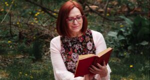 older white woman reading a book on blanket on the grass