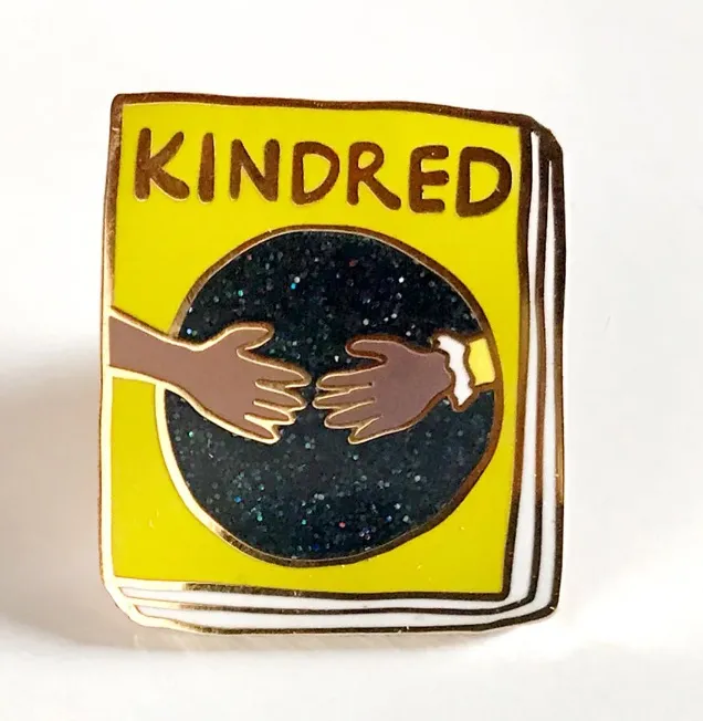Image of a yellow book-shaped pin. It is the cover of Kindred.