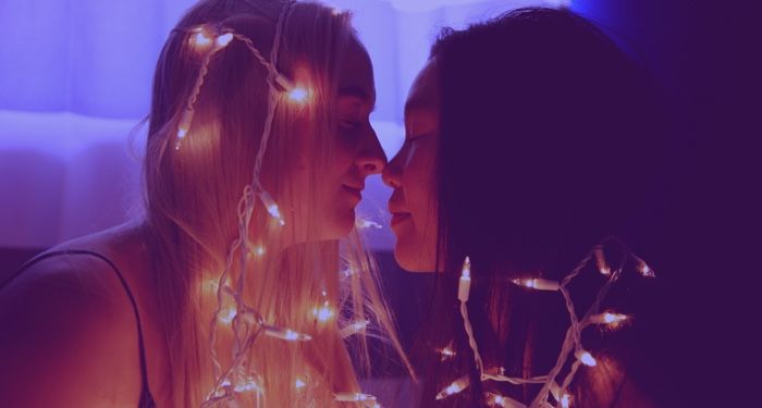 an Asian and a white woman snuggling with lights around them