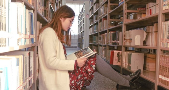 fair-skinned Asian woman sitting on the floor of a library reading