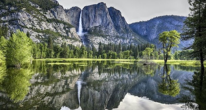 a photo of a mountain and waterfall reflected in a lake