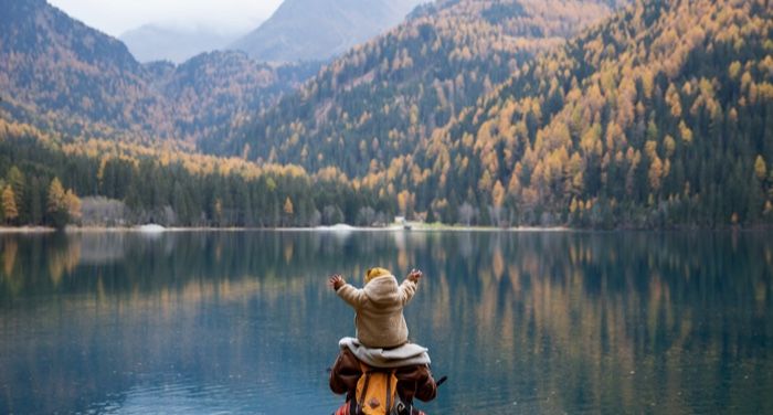 kid on adults' shoulder in front of scenic lake