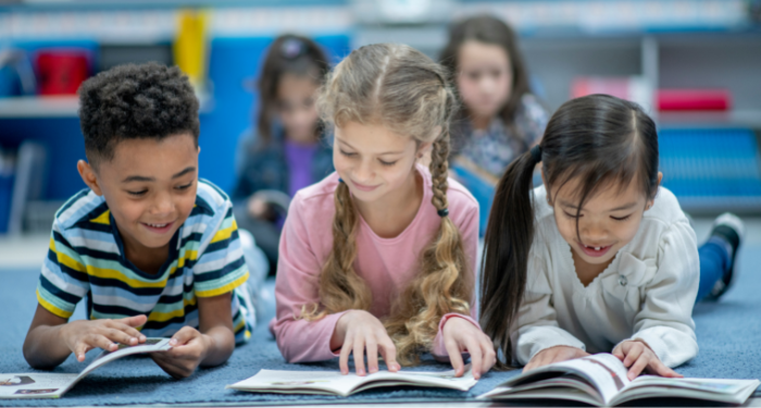 a photo of three kids on the floor reading. They are smiling