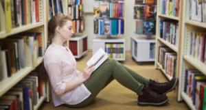 a photo of a white teenage girl sitting on the floor of a bookstore reading